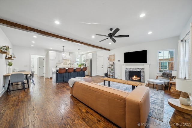 living room with a fireplace, beamed ceiling, sink, ceiling fan, and dark wood-type flooring