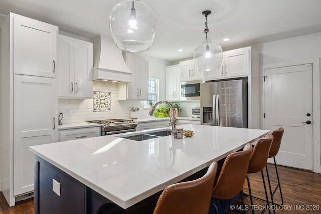 kitchen featuring decorative light fixtures, stainless steel appliances, an island with sink, and decorative backsplash