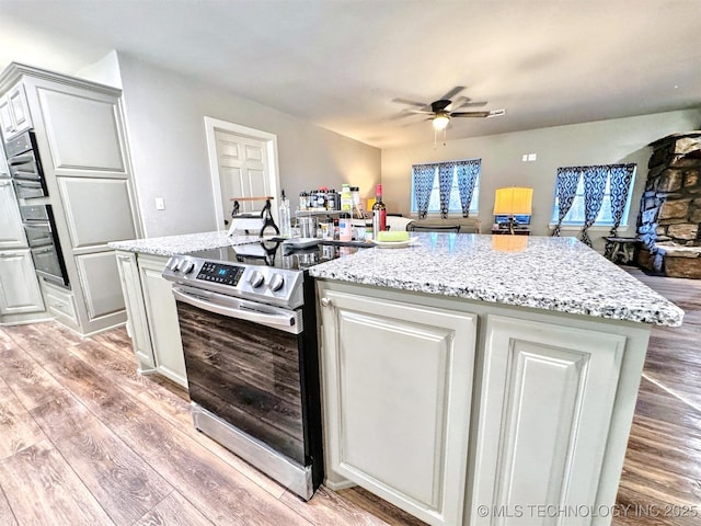 kitchen with a center island, a ceiling fan, light wood-style floors, stainless steel electric range, and light stone countertops