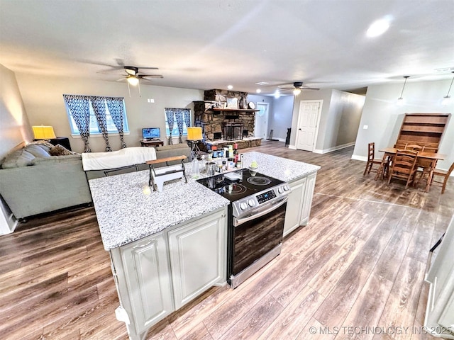 kitchen with electric stove, light wood-style floors, open floor plan, white cabinetry, and light stone countertops