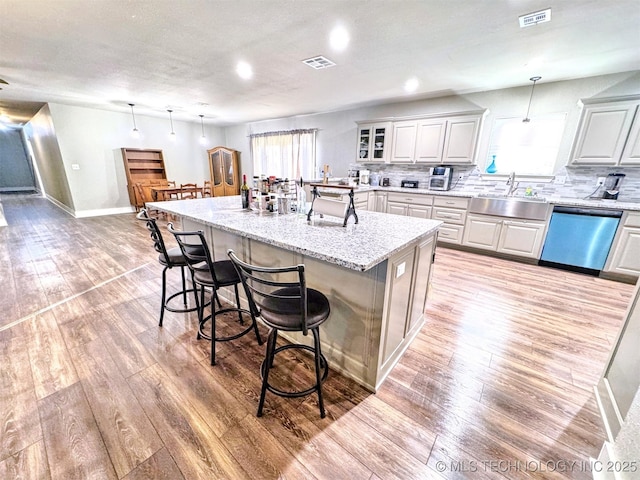 kitchen with a breakfast bar, visible vents, light wood-style floors, a sink, and dishwasher