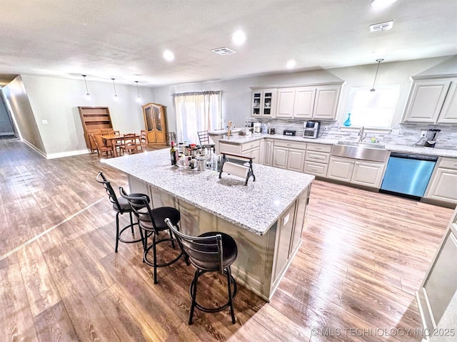 kitchen featuring visible vents, light wood-style flooring, a kitchen island, a sink, and dishwasher