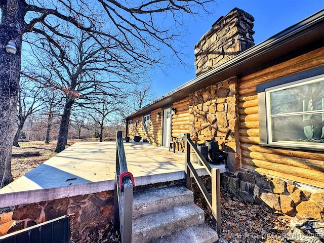 view of side of home with log exterior, a chimney, and a wooden deck