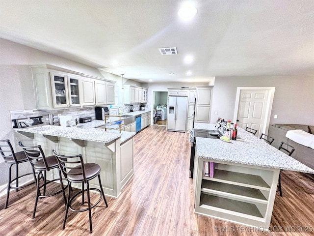 kitchen with visible vents, white fridge with ice dispenser, a peninsula, light wood-style floors, and a kitchen bar