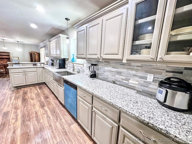 kitchen featuring light wood finished floors, hanging light fixtures, decorative backsplash, a sink, and dishwashing machine