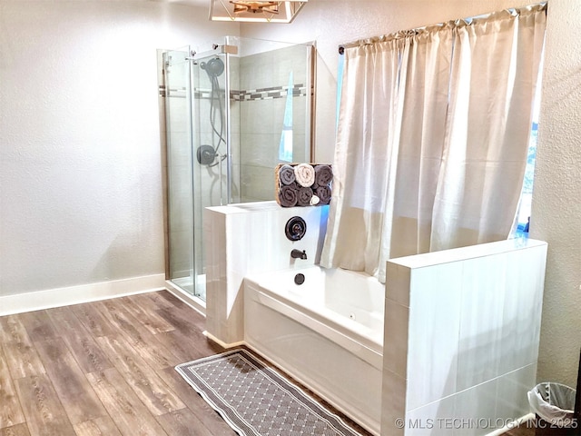 bathroom with baseboards, a textured wall, wood finished floors, a shower stall, and a bath