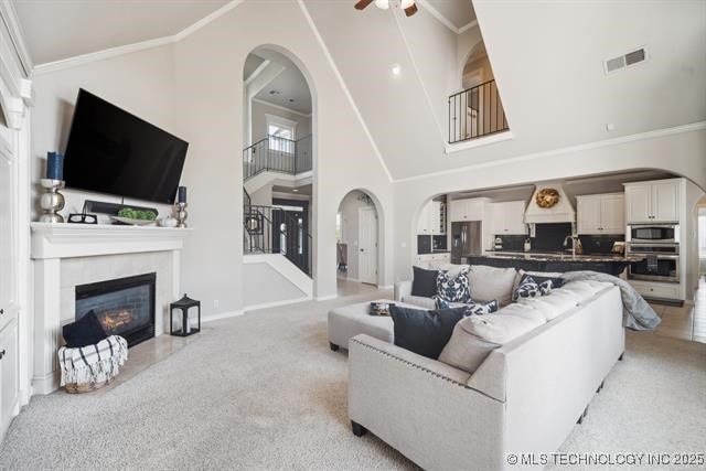 living room featuring a fireplace, high vaulted ceiling, ornamental molding, ceiling fan, and light carpet