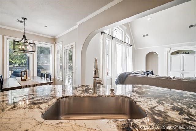 interior details with sink, crown molding, a chandelier, stone counters, and pendant lighting