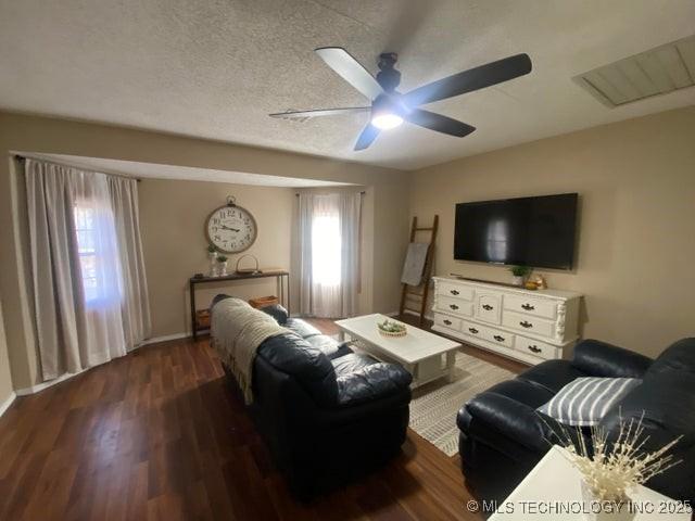 living room with dark wood-type flooring, ceiling fan, and a textured ceiling