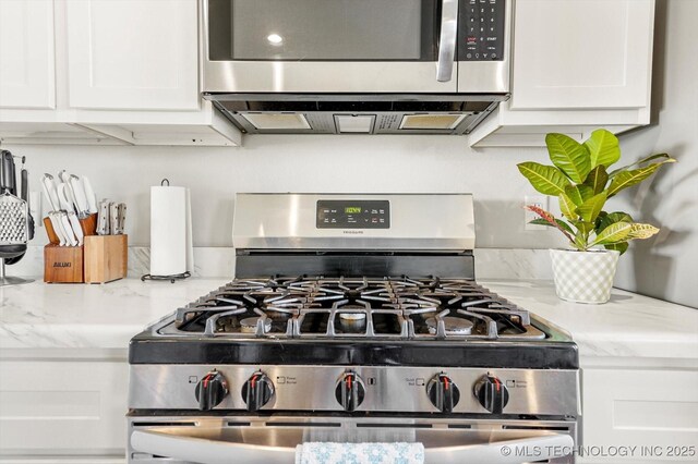 room details featuring stainless steel appliances, light stone countertops, and white cabinets