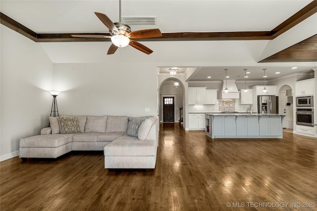 unfurnished living room with beam ceiling, dark wood-type flooring, and ceiling fan