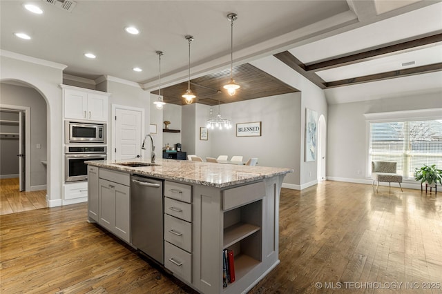 kitchen with sink, a kitchen island with sink, hanging light fixtures, stainless steel appliances, and light stone countertops