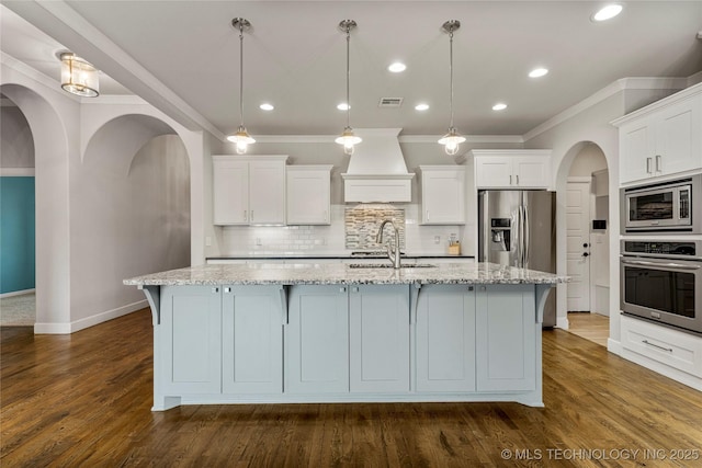 kitchen with white cabinetry, appliances with stainless steel finishes, decorative light fixtures, and a kitchen island with sink