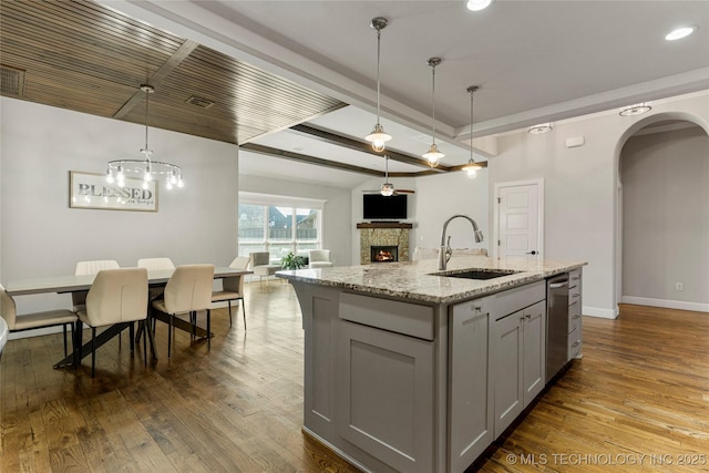 kitchen with sink, light stone counters, decorative light fixtures, a center island with sink, and gray cabinets