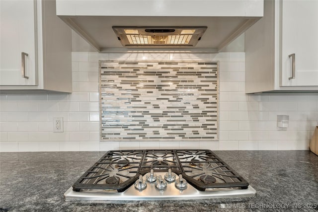 kitchen with stainless steel gas stovetop, exhaust hood, backsplash, and dark stone counters