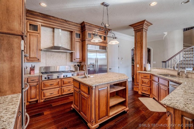 kitchen with sink, hanging light fixtures, stainless steel appliances, an island with sink, and wall chimney exhaust hood