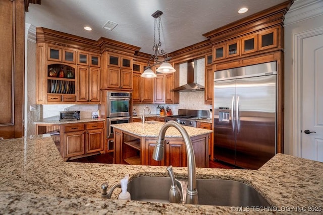 kitchen featuring sink, hanging light fixtures, light stone counters, stainless steel appliances, and wall chimney range hood