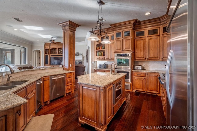 kitchen featuring sink, hanging light fixtures, appliances with stainless steel finishes, dark hardwood / wood-style flooring, and an island with sink