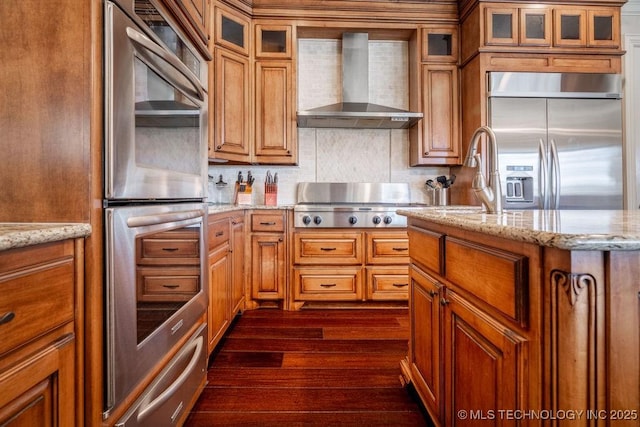 kitchen featuring wall chimney range hood, decorative backsplash, stainless steel appliances, and light stone countertops