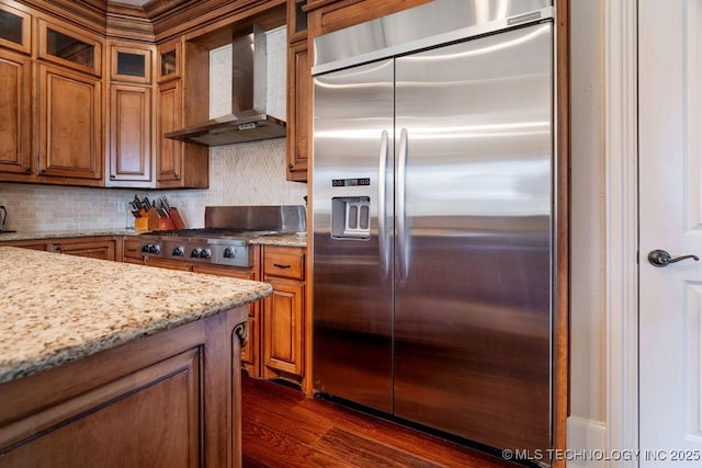 kitchen with appliances with stainless steel finishes, dark hardwood / wood-style flooring, light stone countertops, decorative backsplash, and wall chimney range hood