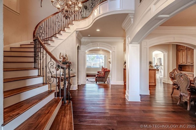 foyer entrance with an inviting chandelier, a towering ceiling, ornamental molding, and dark hardwood / wood-style flooring