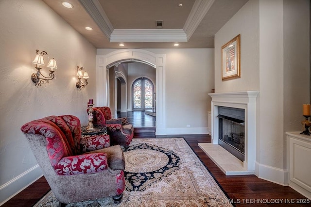 interior space with a tiled fireplace, ornamental molding, dark hardwood / wood-style flooring, and a tray ceiling