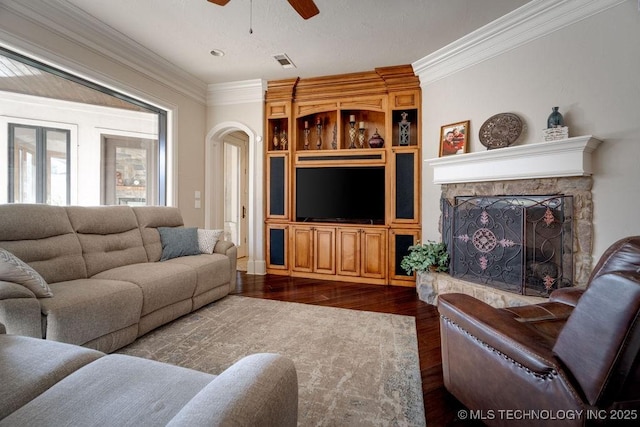 living room featuring ceiling fan, a stone fireplace, crown molding, and dark hardwood / wood-style flooring