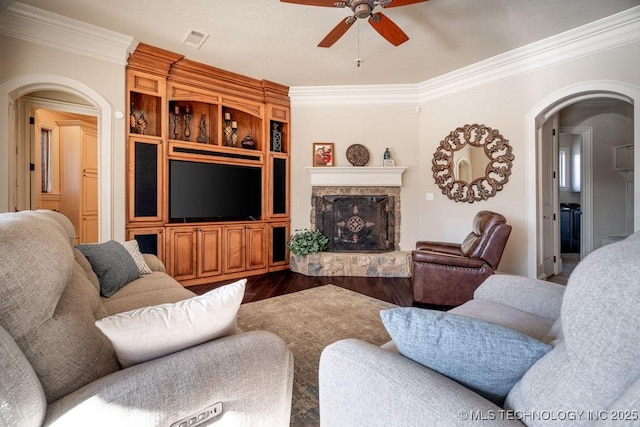 living room with crown molding, a stone fireplace, wood-type flooring, and ceiling fan