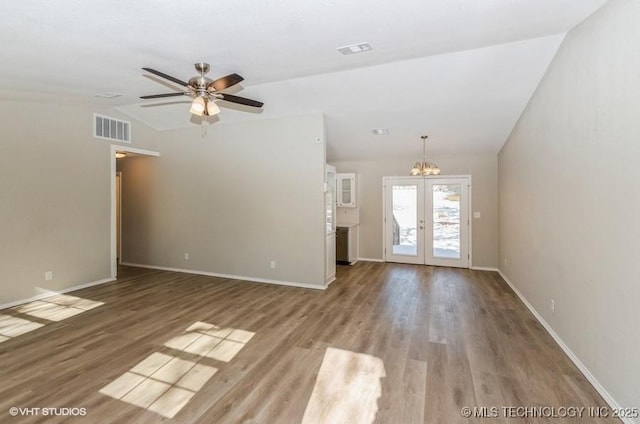 unfurnished living room featuring hardwood / wood-style flooring, vaulted ceiling, ceiling fan with notable chandelier, and french doors