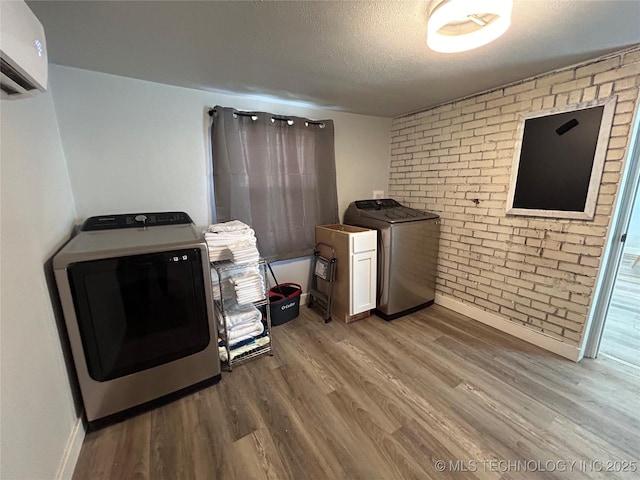 laundry room featuring hardwood / wood-style floors, washing machine and dryer, cabinets, a textured ceiling, and an AC wall unit