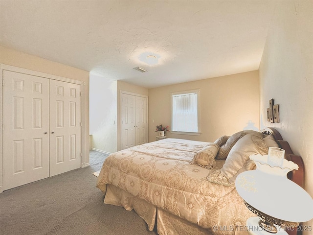 bedroom with two closets, a textured ceiling, and carpet flooring