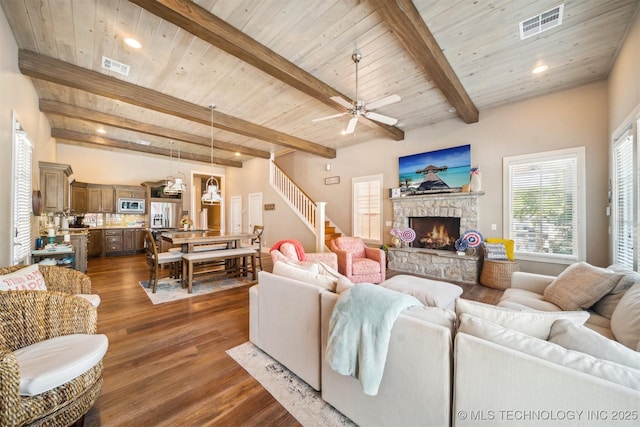 living room featuring a stone fireplace, wood ceiling, dark hardwood / wood-style floors, ceiling fan, and beam ceiling