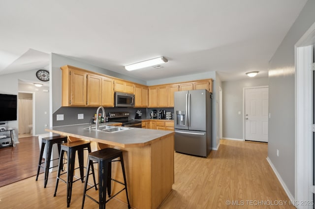 kitchen featuring appliances with stainless steel finishes, sink, a kitchen breakfast bar, light brown cabinets, and light hardwood / wood-style flooring