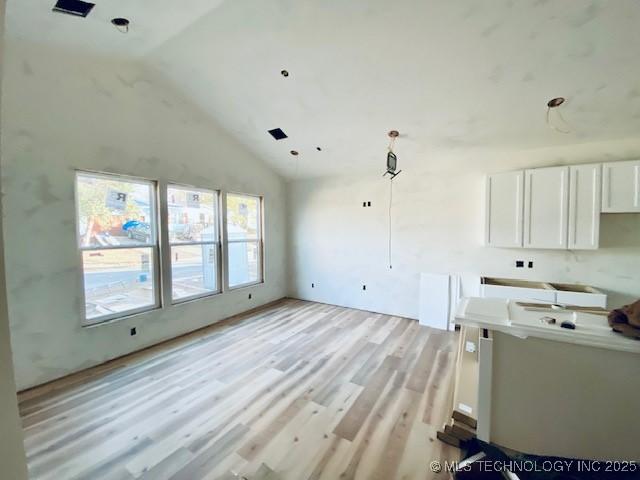 kitchen with light wood-type flooring, decorative light fixtures, high vaulted ceiling, and white cabinets