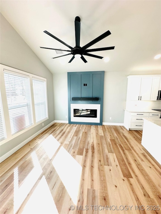 unfurnished living room with light wood-type flooring, a fireplace, baseboards, ceiling fan, and vaulted ceiling