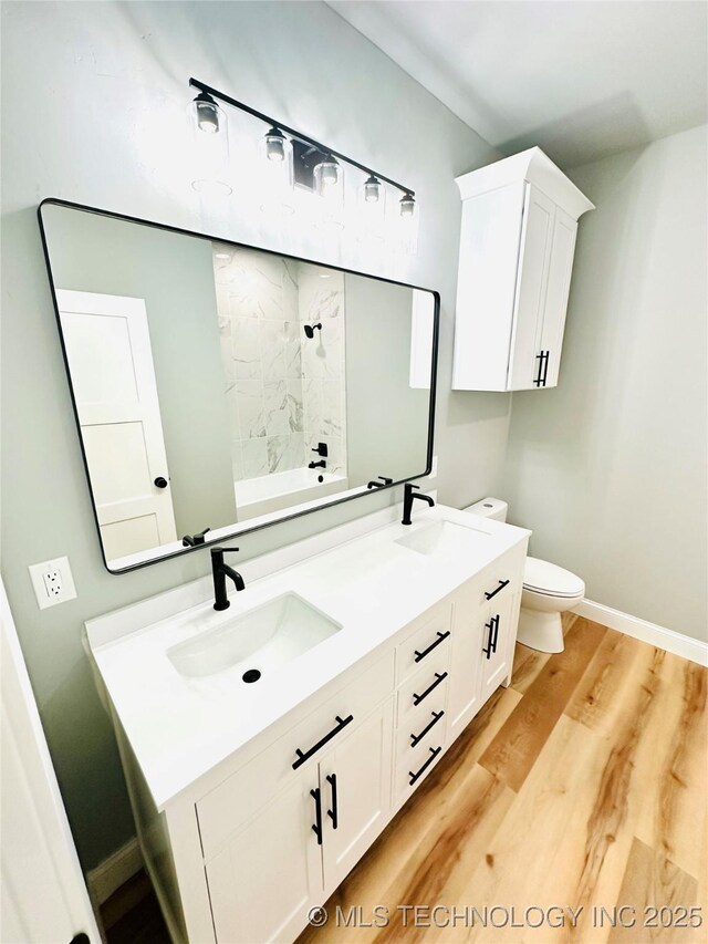 bathroom with a sink, toilet, wood finished floors, and double vanity
