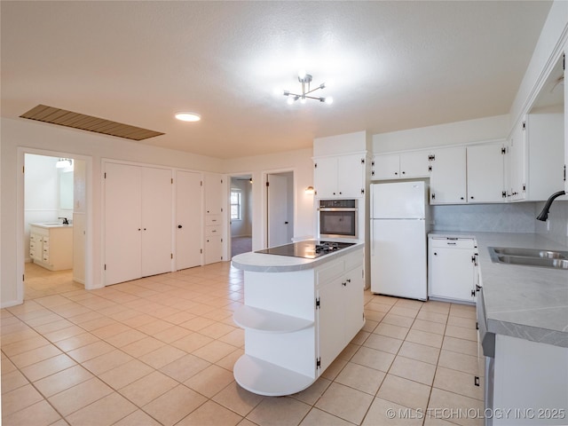 kitchen with sink, white cabinetry, a kitchen island, stainless steel oven, and white fridge