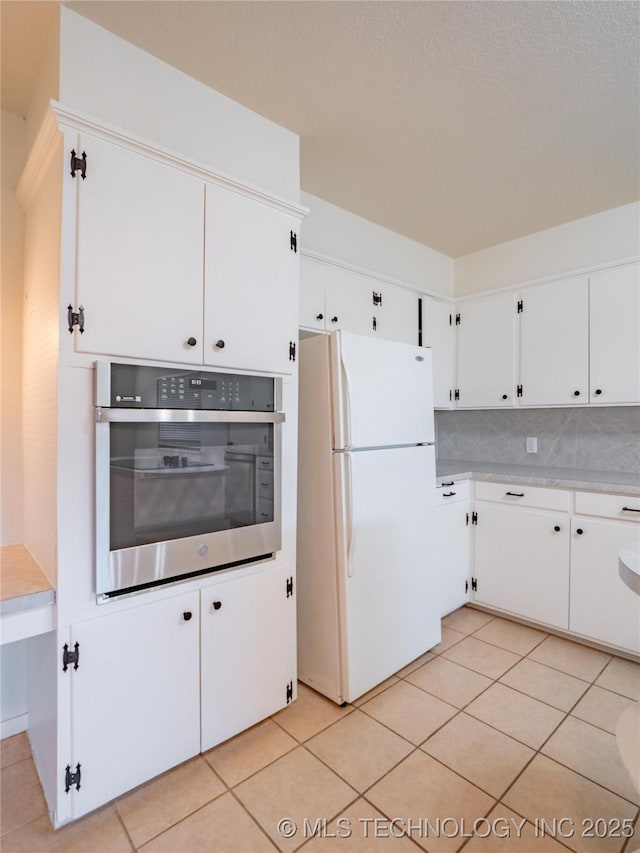 kitchen with white refrigerator, tasteful backsplash, white cabinets, light tile patterned flooring, and stainless steel oven