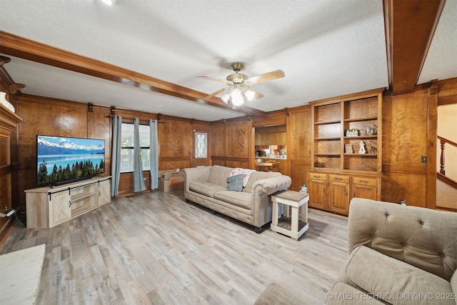 living room featuring wooden walls, beamed ceiling, ceiling fan, a textured ceiling, and light hardwood / wood-style flooring