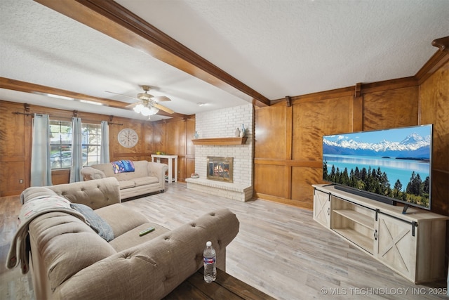 living room featuring a fireplace, wooden walls, ceiling fan, a textured ceiling, and light hardwood / wood-style flooring