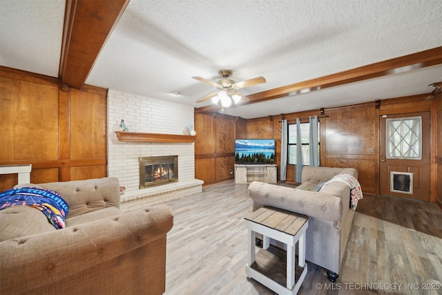 living room with a textured ceiling, light hardwood / wood-style floors, a brick fireplace, and wood walls