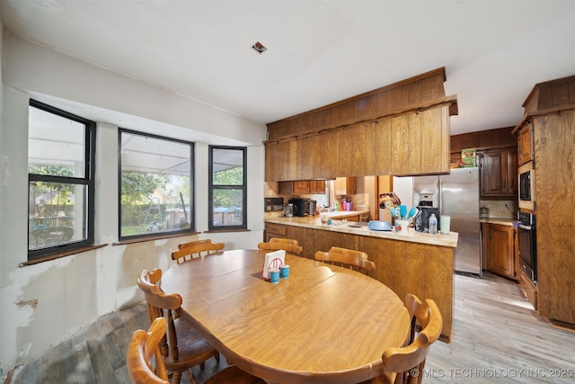 kitchen featuring stainless steel appliances, kitchen peninsula, light hardwood / wood-style floors, and plenty of natural light