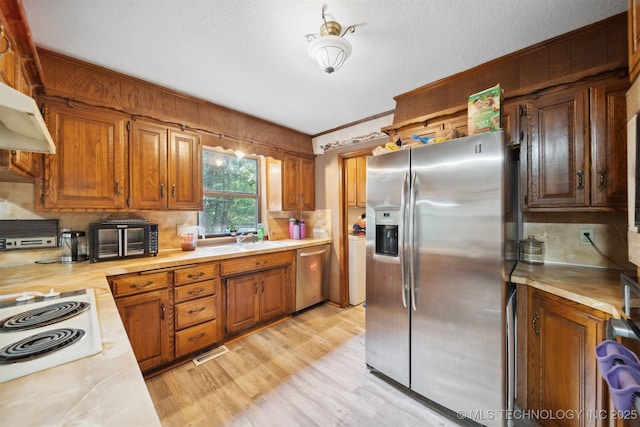 kitchen with appliances with stainless steel finishes, range hood, sink, ornamental molding, and light hardwood / wood-style floors