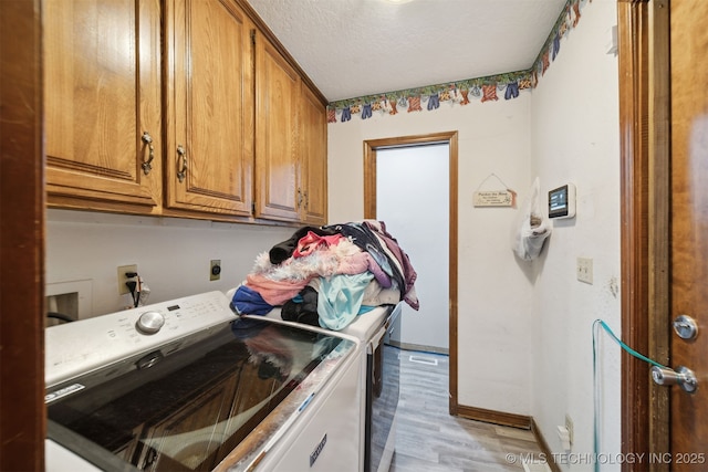 clothes washing area with cabinets, washer and dryer, a textured ceiling, and light wood-type flooring