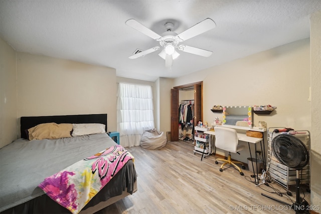 bedroom featuring light hardwood / wood-style flooring, ceiling fan, a textured ceiling, a walk in closet, and a closet