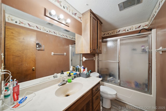 full bathroom with hardwood / wood-style flooring, bath / shower combo with glass door, vanity, a textured ceiling, and toilet