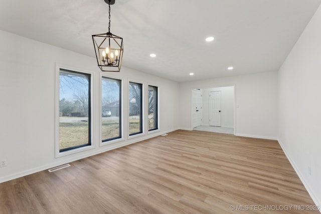 spare room featuring a chandelier and light hardwood / wood-style flooring