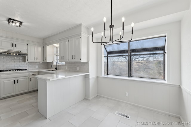 kitchen featuring sink, kitchen peninsula, white cabinets, pendant lighting, and backsplash