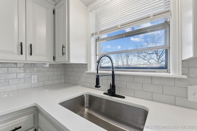 kitchen with tasteful backsplash, white cabinetry, and sink