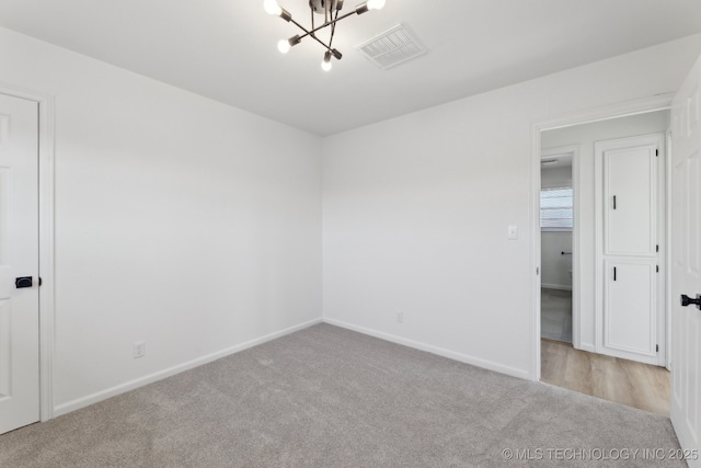 empty room with an inviting chandelier and light colored carpet